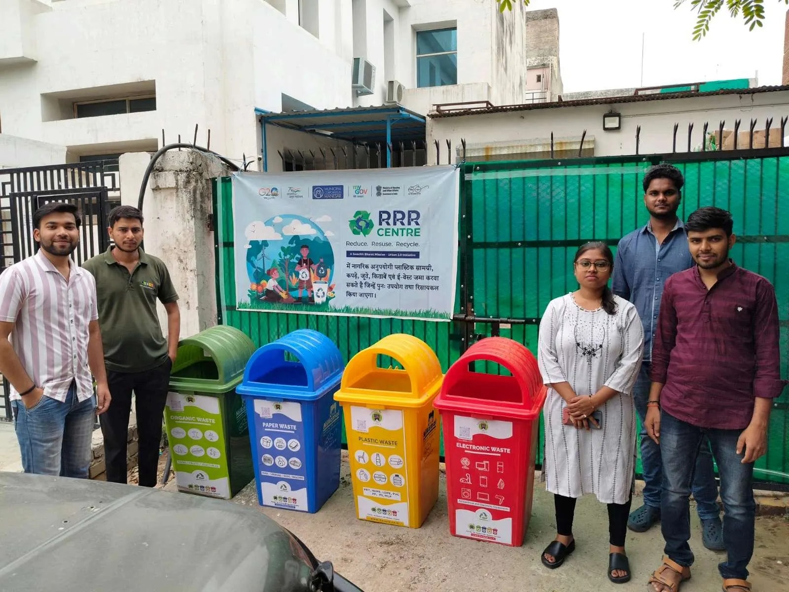 Team standing beside green, blue, yellow and red bins at a gate