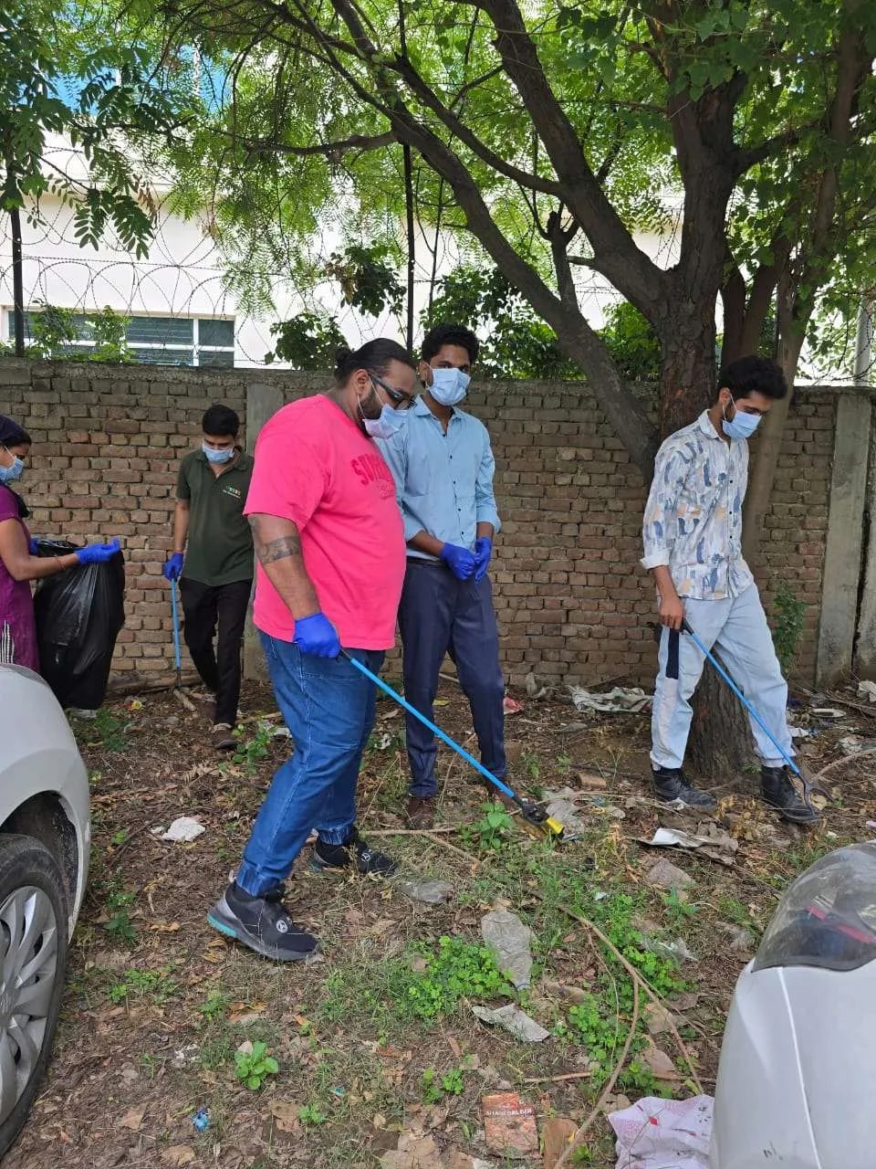 Volunteers with gloves and pickers collecting litter beside a wall