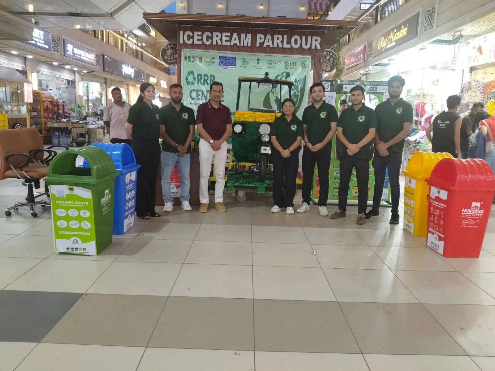 Team in green shirts lined up in front of an RRR Centre with bins